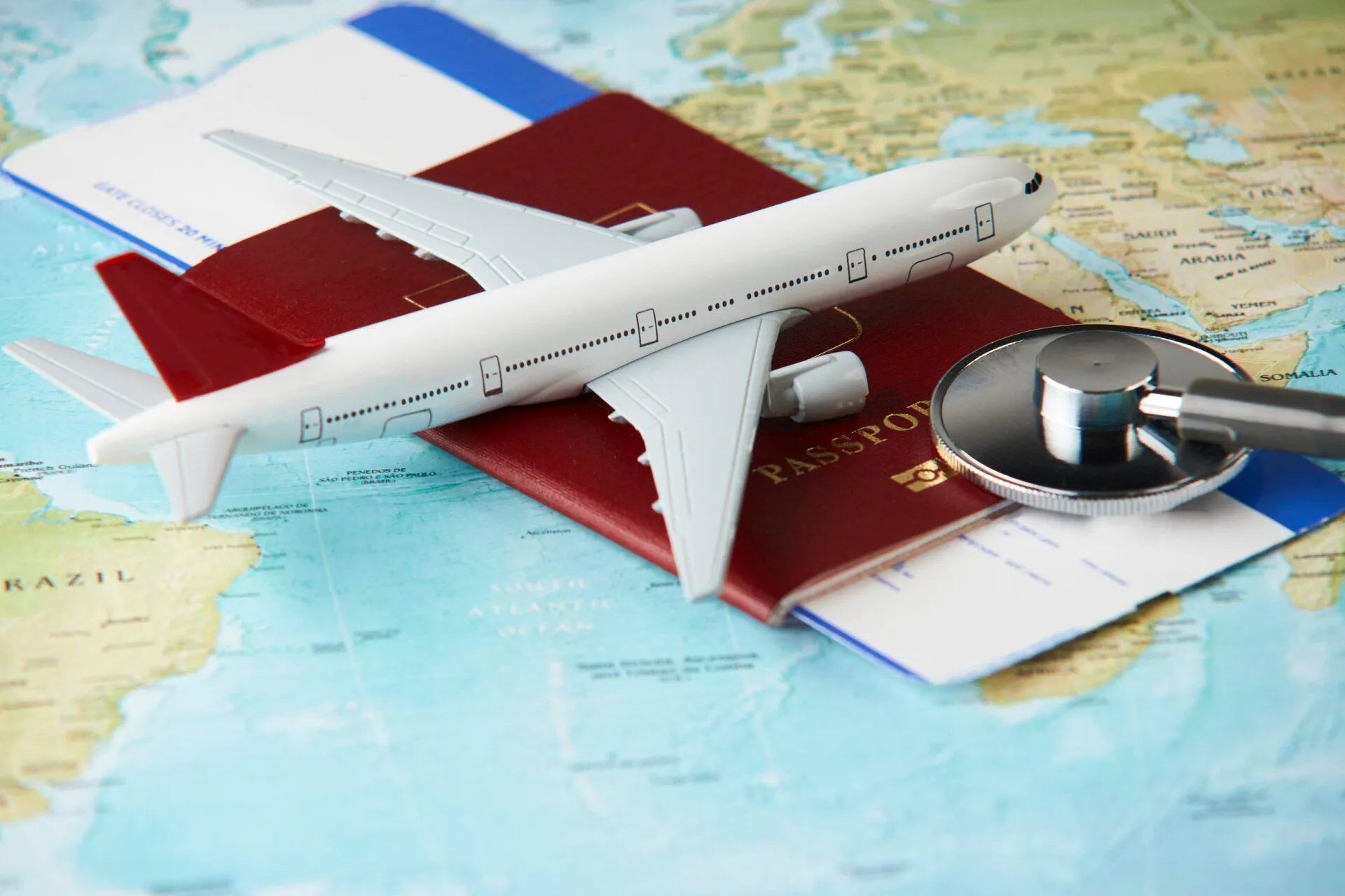 Modellflugzeug, Reisepass, Bordkarte und Stethoskop auf einer Weltkarte